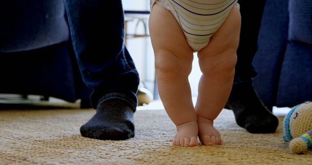 A toddler takes tentative steps beside an adult's feet, symbolizing early childhood development and the support of family. It captures a milestone moment of a child learning to walk, with the comfort of a caregiver close by.