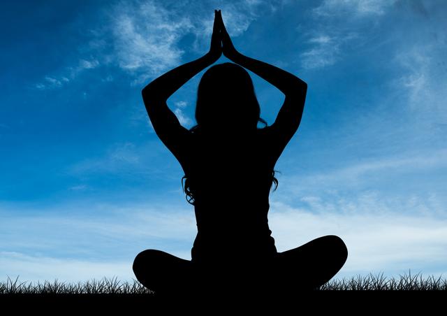 Silhouette of woman meditating in yoga pose on grass with blue sky backdrop. Ideal for illustrating concepts of tranquility, mindfulness, healthy lifestyle, wellness retreats, nature connection, and meditation practices.