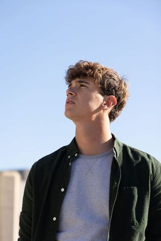 Late teen male gazing upward on rooftop under clear blue sky sunlit urban portrait