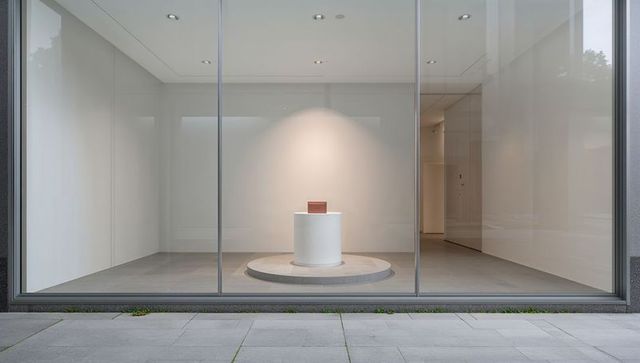 Minimalist storefront gallery showcasing single brown box on illuminated white pedestal