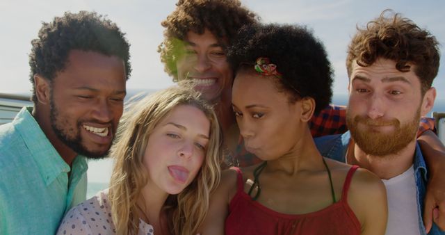 Happy diverse male and female friends making funny faces and taking selfies on sunny beach. Summer, vacations, friendship, fun, social media, communication, togetherness and relaxation, unaltered.