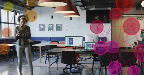 Mid adult woman using smartphone in modern coworking space with digital network overlay