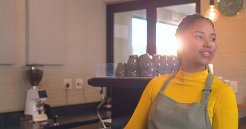 Smiling african american barista serving espresso in minimalist cafe with sun flare