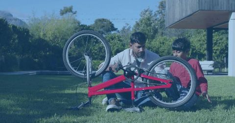 Repairing red bicycle with son on lawn teaching bike maintenance and father-son bonding