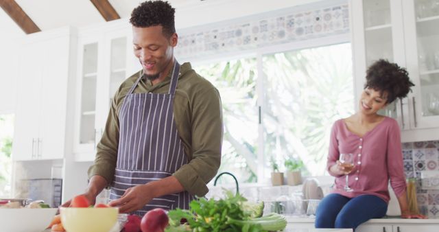 Happy african american couple cooking and drinking wine in kitchen. Spending quality time at home together concept.