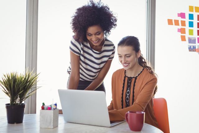 Smiling female executives using laptop in creative office