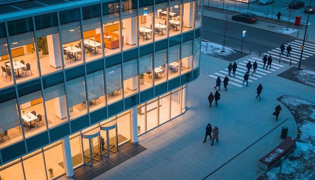 Evening glass office tower with revolving doors and winter pedestrians crossing plaza