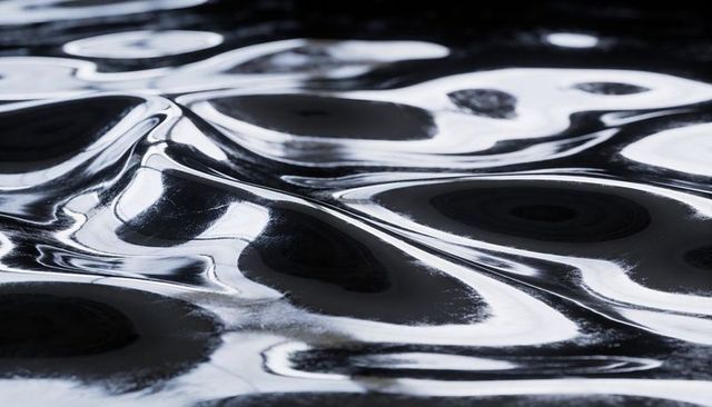 Shimmering reflective rippled metallic liquid with glossy mirrorlike highlights monochrome
