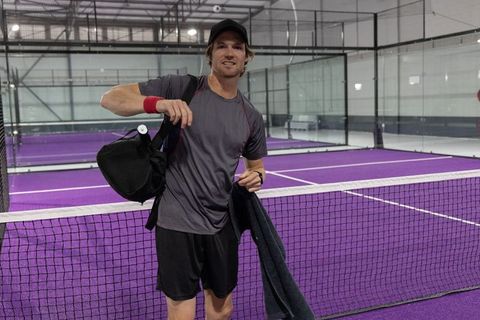 Padel player leaving court carrying duffel bag and towel on vibrant purple indoor court