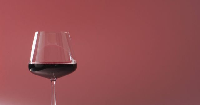 Depicting a sophisticated and elegant wine glass filled partially with red wine set against a simple pink background. Perfect for use in advertisements, blogs, or magazines related to wine tasting, beverages, fine dining, and culinary arts.
