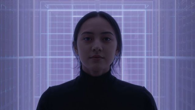 Woman standing in symmetrical neon grid tunnel wearing black turtleneck facing forward
