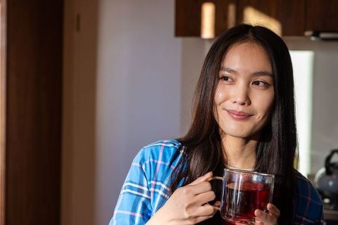 Asian Woman Holding Mug of Red Tea in Cozy Kitchen Setting