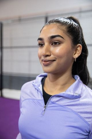 Indian woman athlete posing in lavender quarter-zip on indoor purple court, calm confident