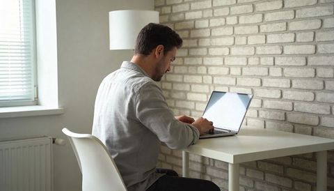 Man working on laptop in minimalist home office with exposed brick wall