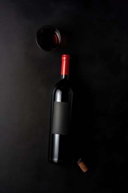 Elegant bottle of red wine lying on a black background with a cork and glass of red wine. Ideal for use in advertising for luxury beverages, wine reviews, or restaurant menus.