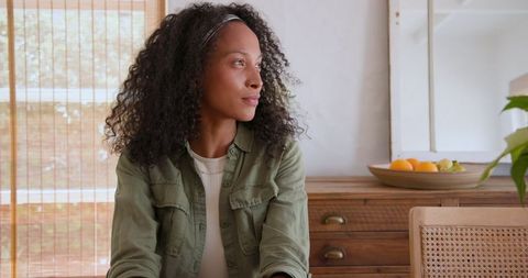 Woman Gazing Thoughtfully at Home Near Bamboo Blinds