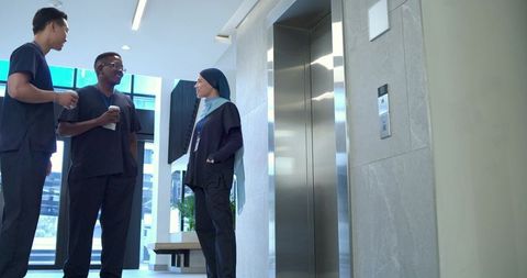 Clinic staff chatting in modern lobby near elevator wearing scrubs and holding coffee