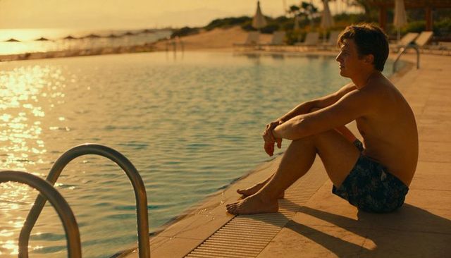 Man sitting by resort pool at sunset gazing in solitude during golden hour
