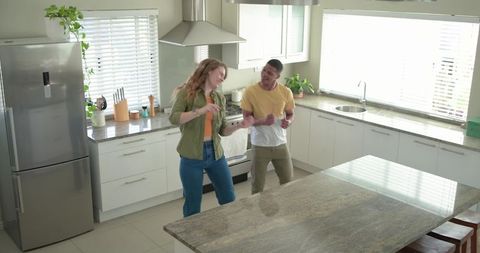 Young couple dancing and laughing in bright modern kitchen with granite island