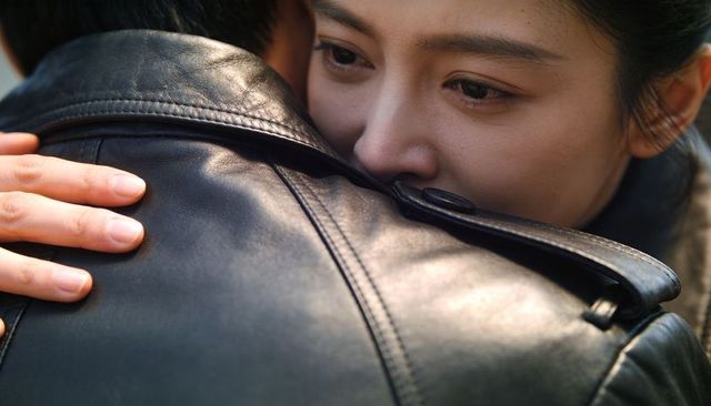 Holding close, woman resting face on partner's shoulder in black leather jacket