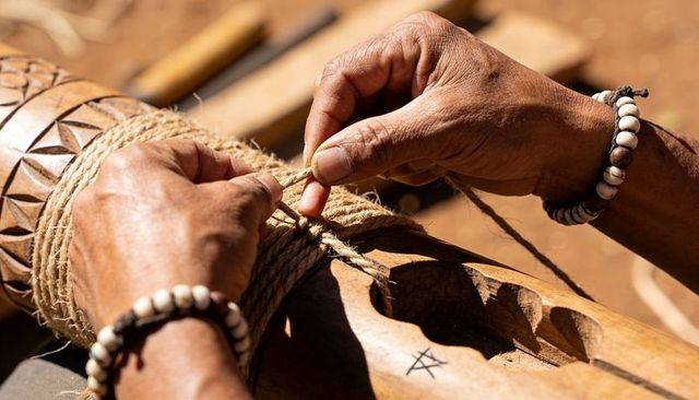 Tying natural twine around carved wooden pole showing handcrafted woodcarving process
