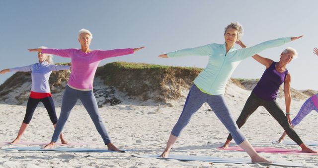 This image shows a group of senior women practicing yoga on the beach. Perfect for use in advertising health and wellness programs, promoting active lifestyles for seniors, or illustrating outdoor sports and exercise activities. The sandy beach and open sky enhance the feeling of freedom and joy in staying active.