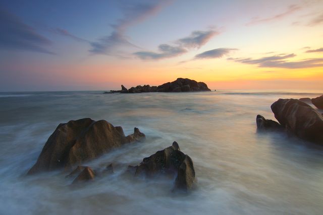 Gentle waves rolling over a rocky shoreline under a dramatic sunset sky. Ideal for use in travel brochures, nature magazines, websites focusing on outdoors, and as background or header images for beach resorts or coastal destination advertisements.