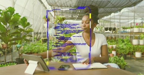 Woman analyzing tablet and taking notes in greenhouse while collecting plant data