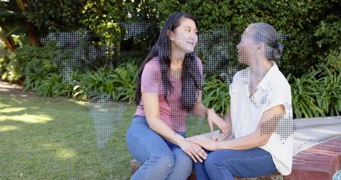 Mother and adult daughter holding hands chatting on brick garden ledge with world map overlay