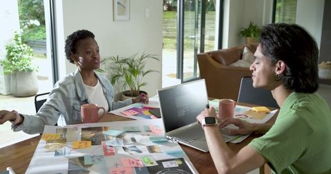 Creative team collaborating over mood board with laptop, reviewing ideas in bright home