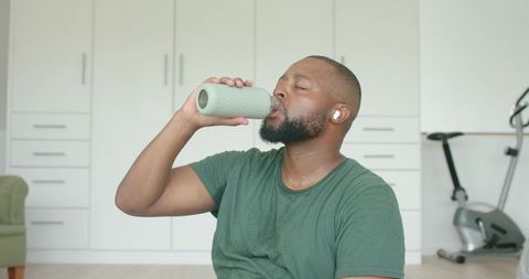 African american man rehydrating after home workout drinking from textured bottle