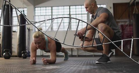Female athlete holding forearm plank while trainer timing workout with dna helix overlay