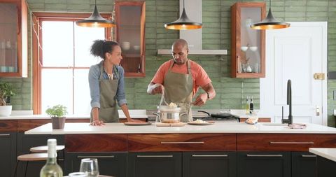 Happy couple cooking together in modern kitchen making pasta