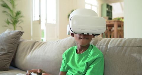 African American Boy Playing VR Game on Couch Wearing White Headset and Holding Controller