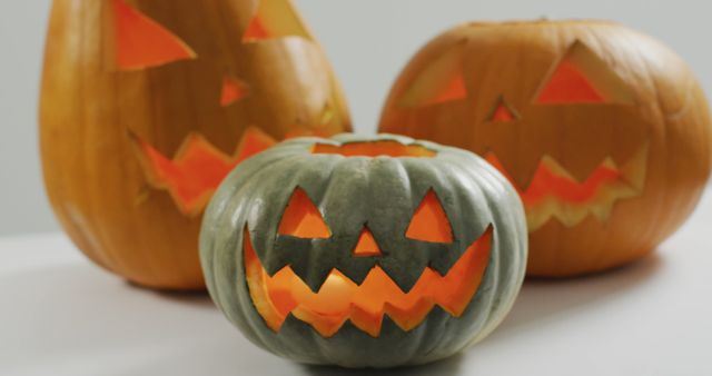 Close-up of three carved pumpkins featuring jack-o'-lantern faces with glowing lights inside. Ideal for use in Halloween-themed advertisements, party invitations, seasonal decor guides, and holiday-related content.