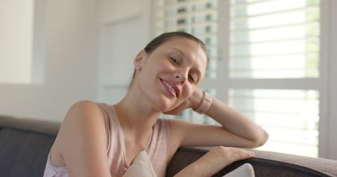 Relaxing woman smiling on sofa in sunlit living room with shutters and soft cushion