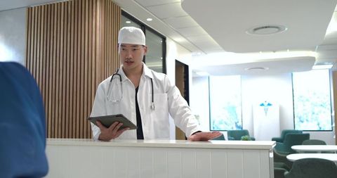 Clinician consulting at reception holding tablet and stethoscope in modern clinic lobby