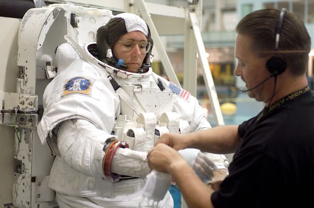 JSC2002-E-22542 (28 May 2002) --- Astronaut Sandra H. Magnus, STS-112 mission specialist, is photographed as the final touches are made on the training version of the Extravehicular Mobility Unit (EMU) space suit prior to being submerged in the waters of the Neutral Buoyancy Laboratory (NBL) near the Johnson Space Center (JSC). United Space Alliance (USA) crew trainer Don Kestler assisted Magnus.