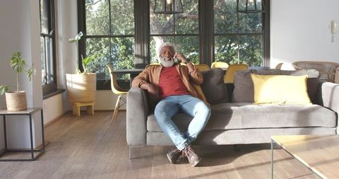 Senior Man Relaxing with Smartphone on Sofa in Sunlit Modern Living Room