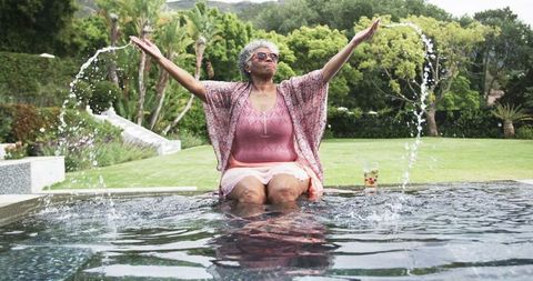Joyful senior woman splashing water in garden pool