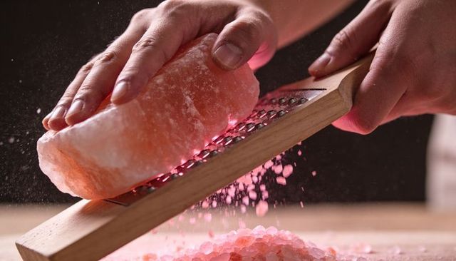 Grating himalayan salt block on wooden grater producing pink salt crystals for culinary use