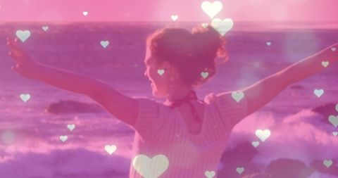 Woman Embraces Sunset by Ocean with Heart Overlays in Dreamlike Scene