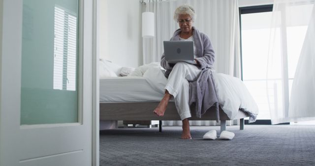 Elderly Woman in Robe Using Laptop on Bed in Minimalist Bedroom - Download Free Stock Images Pikwizard.com