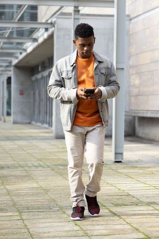 African american student walking on campus checking smartphone under glass canopy