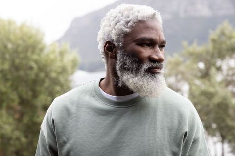 Silver-haired african american man standing contemplative by lakeside wearing green crewneck
