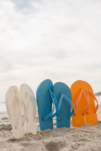 Multi-color flip flops arranged in a row in sand at beach