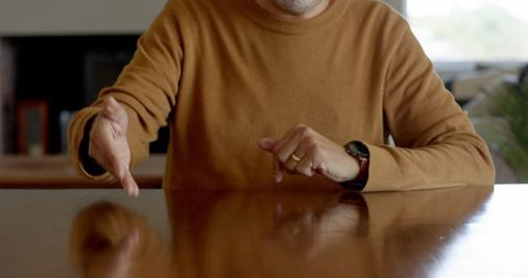 Senior Man Making Gestures at Wooden Table in Casual Setting