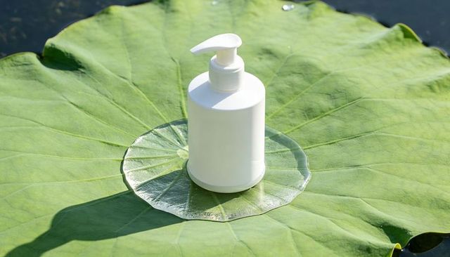 White pump dispenser bottle resting on lotus leaf with wet reflective ring for skincare