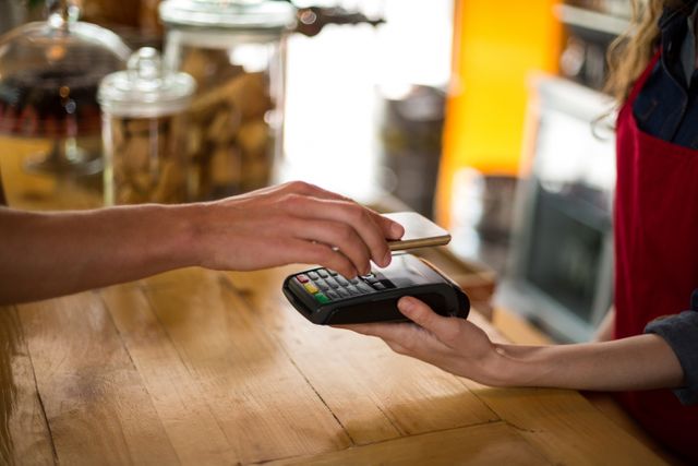 Customer making a contactless payment with a smartphone in a cafe. Ideal for illustrating modern payment methods, digital wallets, and the convenience of cashless transactions. Useful for articles, blogs, and advertisements related to technology, finance, and retail.