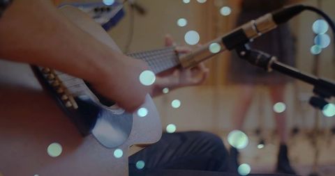 Intimate close-up of guitarist strumming acoustic guitar in recording studio bokeh